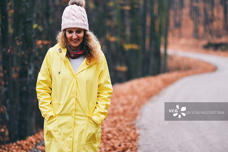 穿着亮黄色雨衣的女士走在落满树叶的秋季森林小路上图片素材