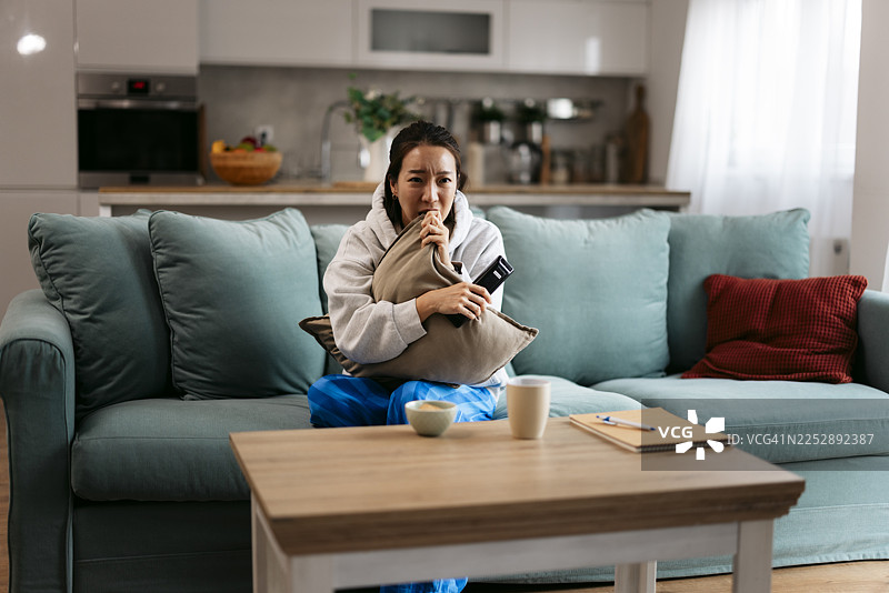 一个女人独自在家看恐怖片时感到害怕图片素材