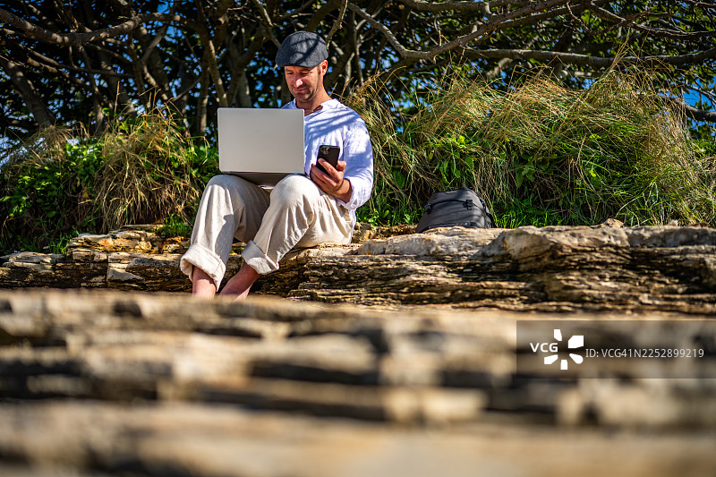 男人在岩石海滩上用笔记本电脑工作图片素材