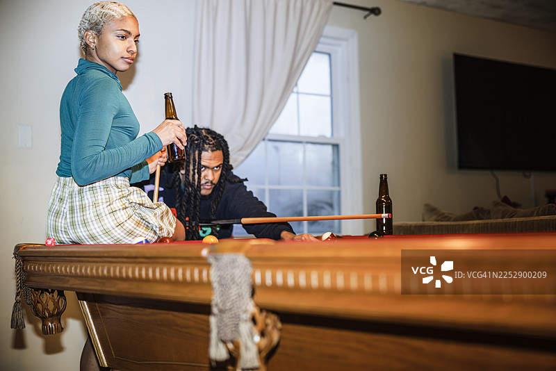 台球之夜。留着胡须的西班牙裔男子和短发女子在放松地玩台球。图片素材