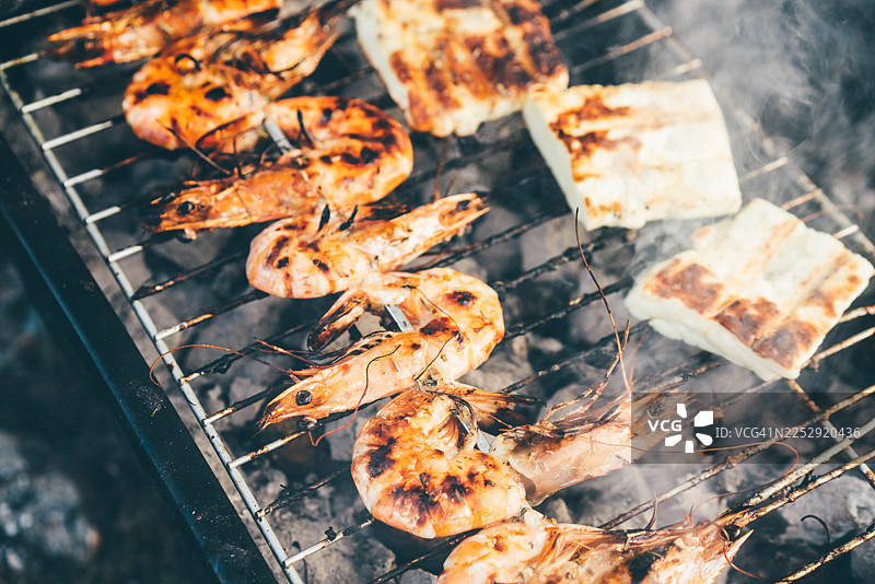 大虾和哈罗米芝士片在炭火烤架上烤制，散发出淡淡的烟熏风味。图片素材