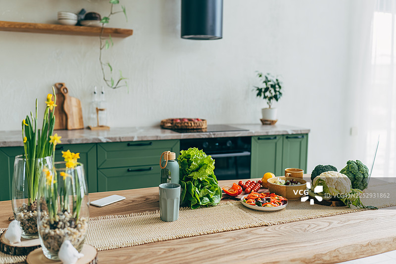 前景是带有大理石台面的空厨房岛，绿色复古台面带抽屉，上方悬挂着吊灯，罐子里放着许多鲜花，背景模糊。图片素材