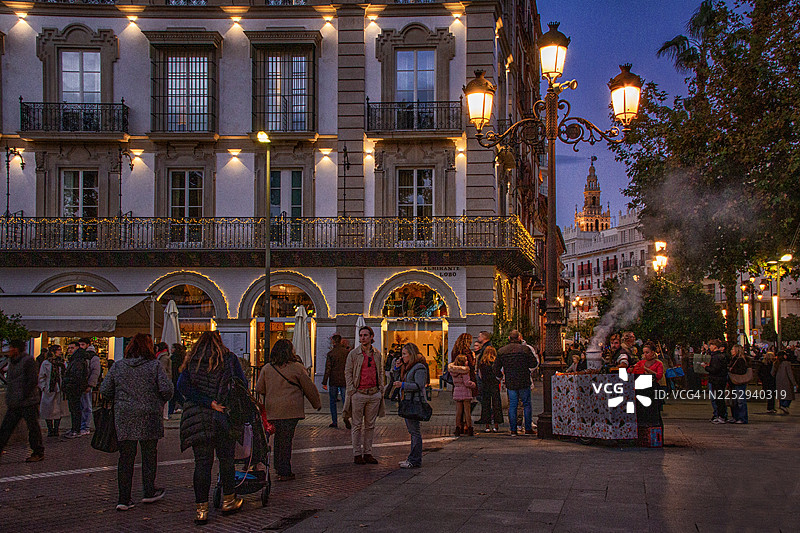 傍晚时分，塞维利亚的吉拉达灯火辉煌，旁边是烤栗子摊和圣诞灯饰。图片素材