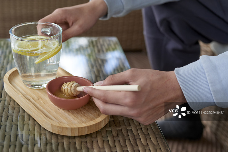 一个人将蜂蜜加入柠檬水中，制作健康饮品图片素材