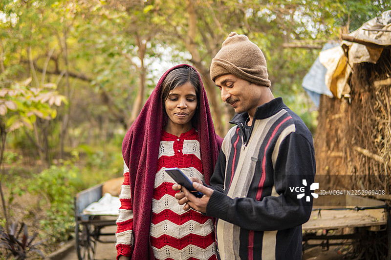 一对快乐的印度乡村已婚夫妇在户外一起使用智能手机的肖像照。图片素材