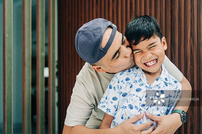 亚洲父亲正在玩耍般地亲吻和拥抱他的儿子图片素材