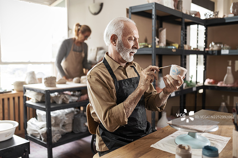 手工艺人工作室场景，一位年长男子正在绘制陶器图片素材