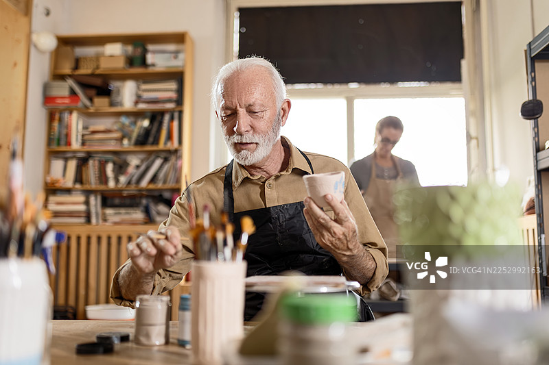 工作室里一位年长的陶艺家正在绘制陶瓷作品图片素材