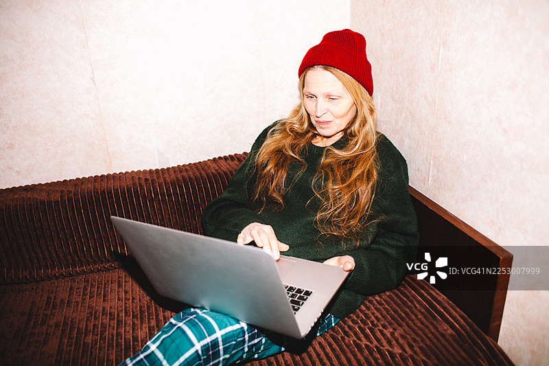 一位快乐的老年女性在家中坐在沙发上使用笔记本电脑图片素材