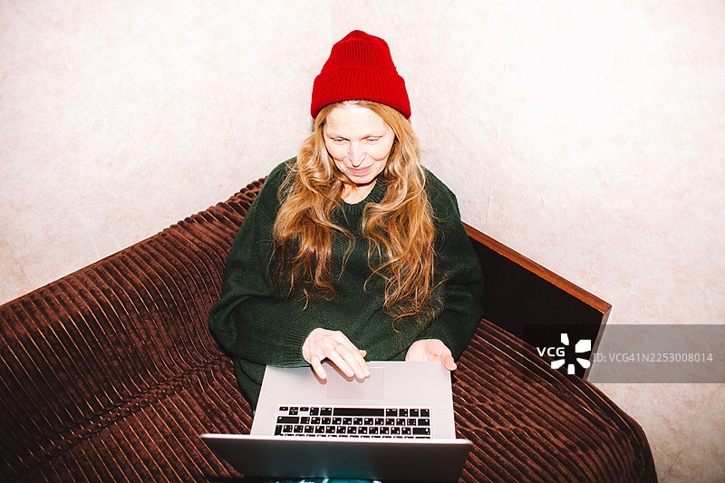 快乐的老年女性在家中沙发上使用笔记本电脑图片素材