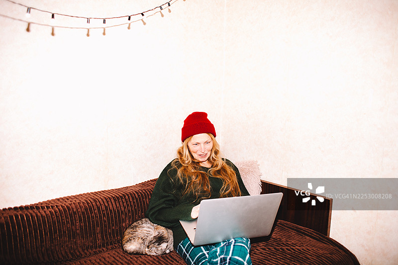 快乐的老年女性在家中坐在沙发上使用笔记本电脑图片素材