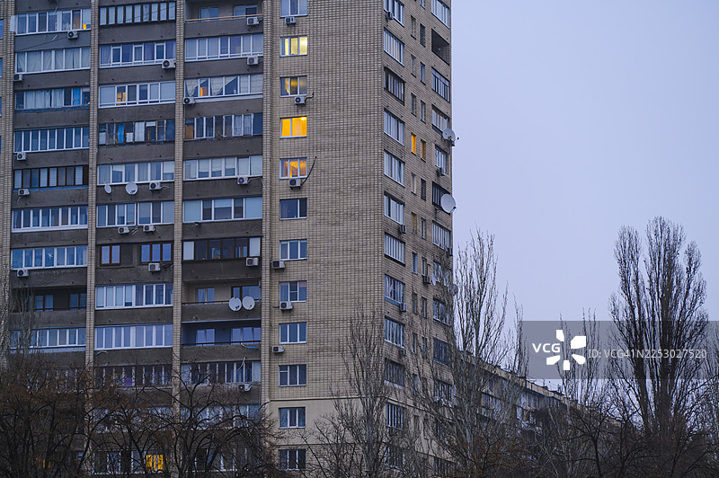 傍晚时分，城市住宅楼的外墙，窗户发出微光图片素材