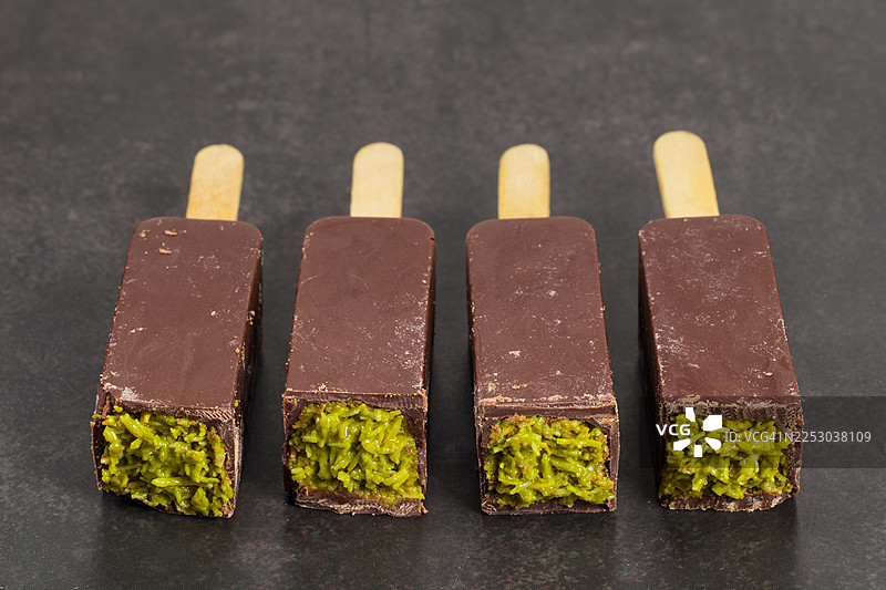 迪拜巧克力，内馅是酥脆的Kataifi面团和开心果酱。插在木棍上。深灰色背景。特写。图片素材