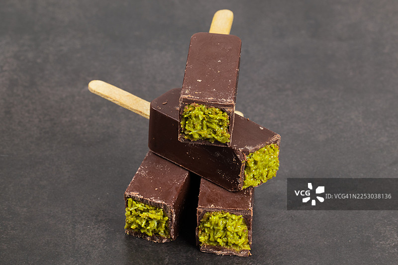纯素迪拜巧克力棒，内填酥脆的 kadaifi 面团和开心果酱，并插有木棍。深灰色背景，特写。图片素材