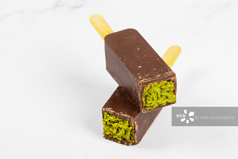 开心果酱的纯素迪拜巧克力棒，内填酥脆的Kataifi面团。带木棍。白背景。特写。图片素材
