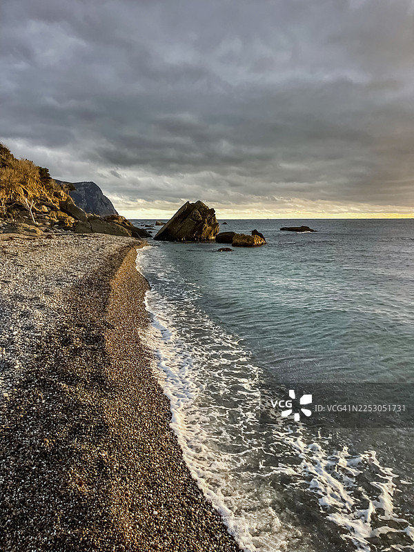地中海海岸线，有鹅卵石海滩、岩石和日落时的壮丽天空图片素材