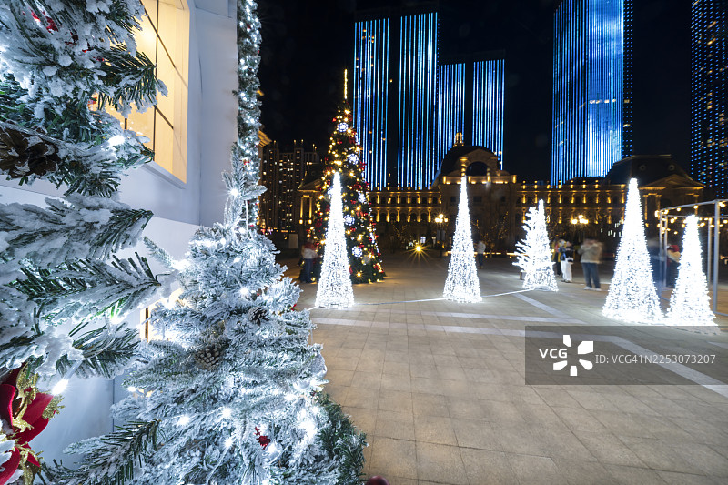 夜晚，现代摩天大楼前装饰着圣诞松树和闪耀的节日树图片素材
