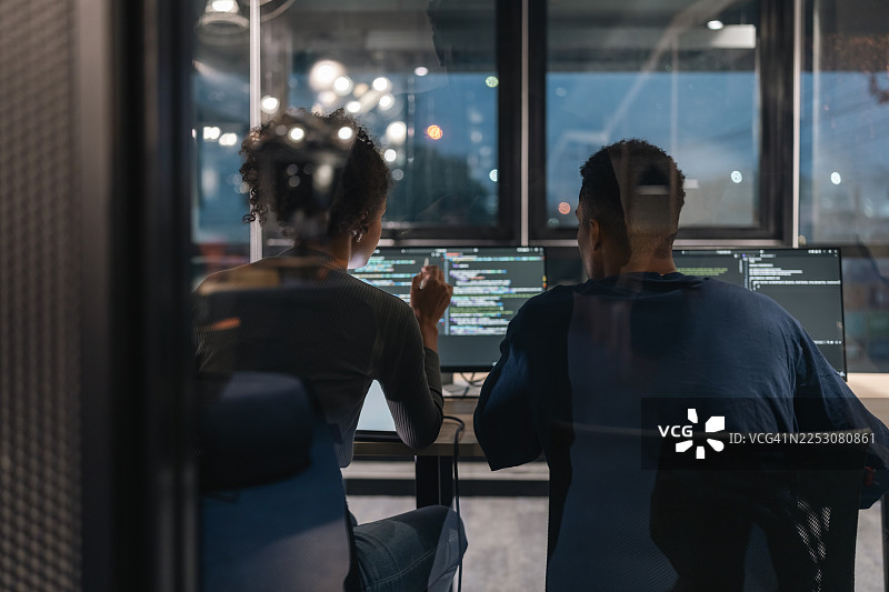 年轻的计算机程序员在夜间于办公室协同工作。图片素材