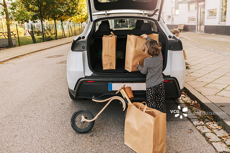 小男孩帮爸爸把购物袋装进汽车后备箱图片素材