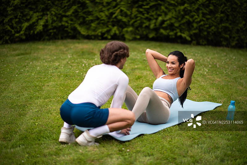 情侣户外锻炼，男士帮助女士做仰卧起坐图片素材
