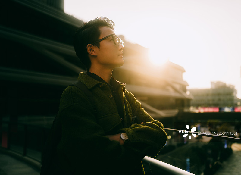 一位自信的年轻亚裔商人抱臂站立在一座现代办公楼前。图片素材