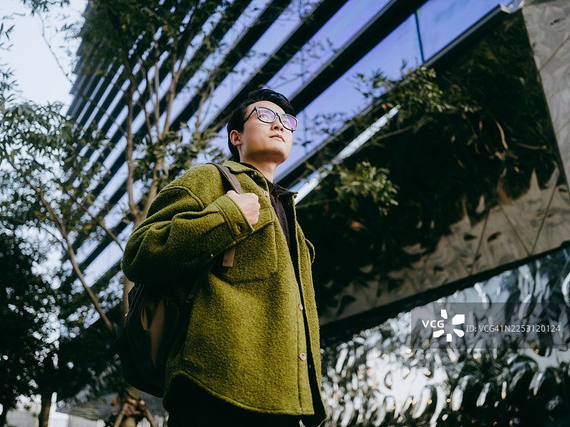 一位自信的年轻亚裔商人站在现代办公楼前。图片素材