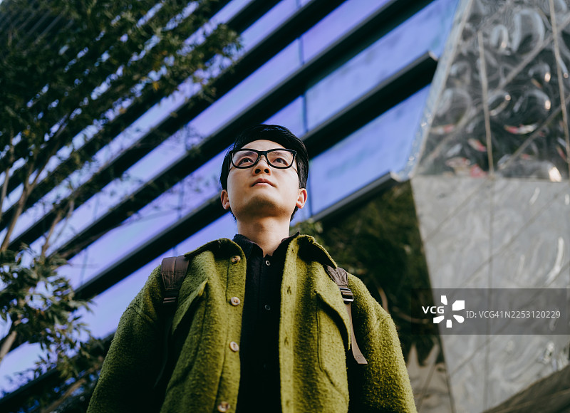 一位自信的年轻亚裔商人站在现代办公楼前。图片素材