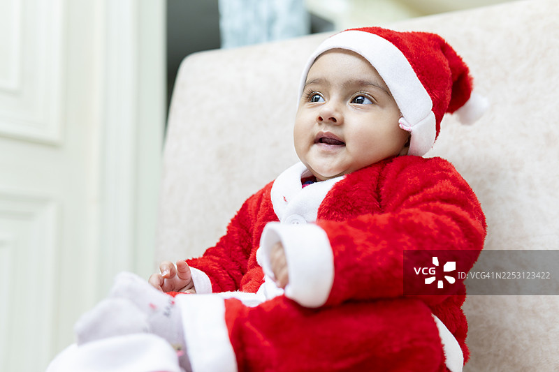 可爱惹人喜爱的微笑女婴，穿着红色圣诞老人服装，在家庆祝圣诞节。图片素材