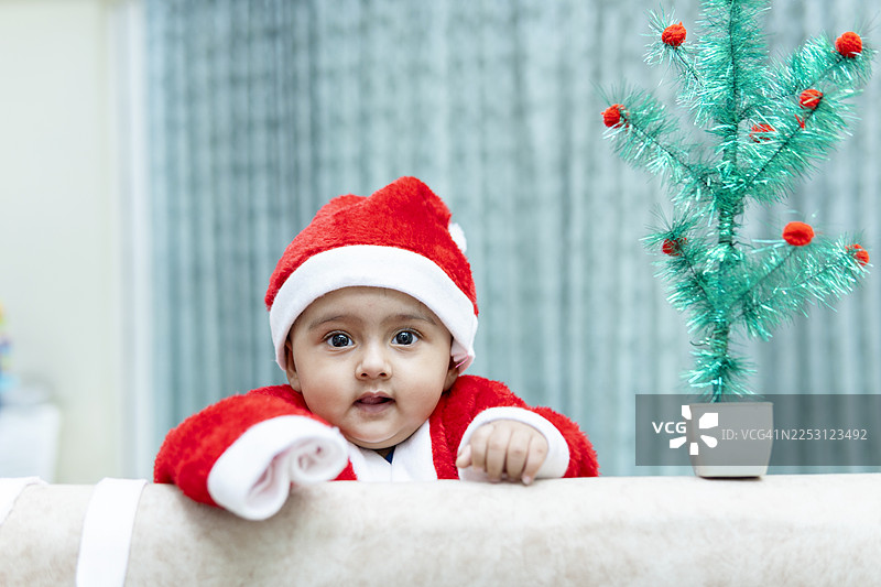 可爱的、惹人喜爱的、面带微笑的婴儿女孩，身穿红色圣诞老人服装，在家庆祝圣诞节。图片素材