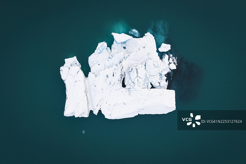 从空中俯瞰，冰岛南部深邃的绿松石水域中漂浮着一块巨大而破碎的纯白冰山，如同冰川杰作，在深邃的大海中格外醒目。图片素材