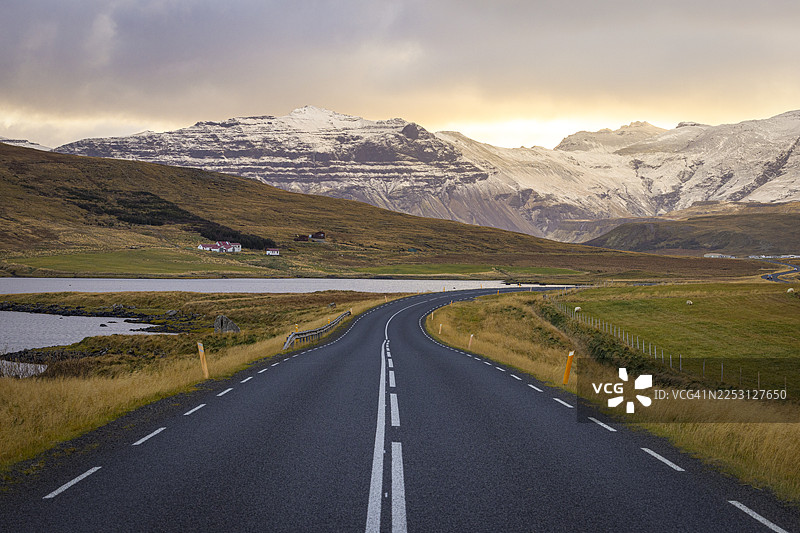 北极黎明的温暖光芒笼罩着冰岛的一条公路，周围是壮丽的雪山，冰岛，欧洲图片素材