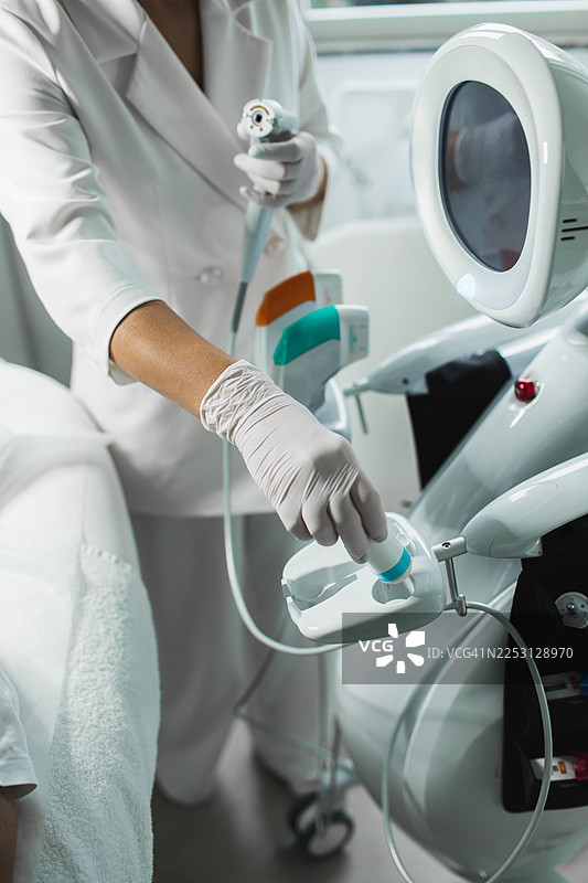 身着无菌手套的皮肤科医生在现代美容诊所使用带有显示器的机器人系统图片素材