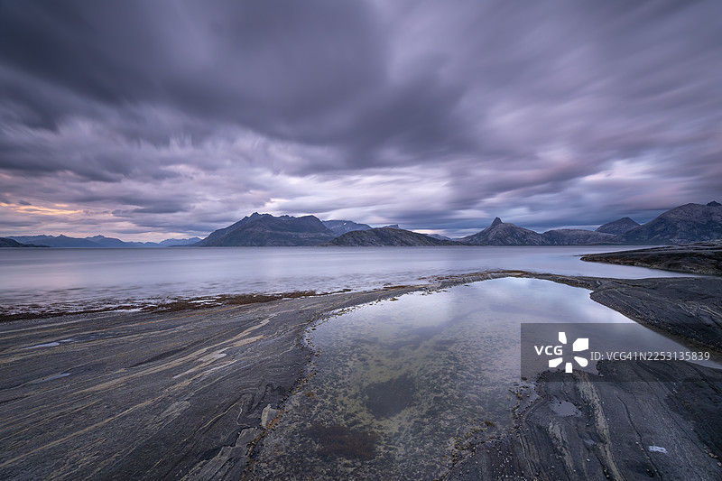 挪威诺德兰郡的韦斯特峡湾在博德附近呈现出戏剧性的氛围。乌云在落日余晖的红黄映衬下闪耀。崎岖的悬崖和山峦倒映在宁静的峡湾中，展现出令人惊叹的洛...图片素材