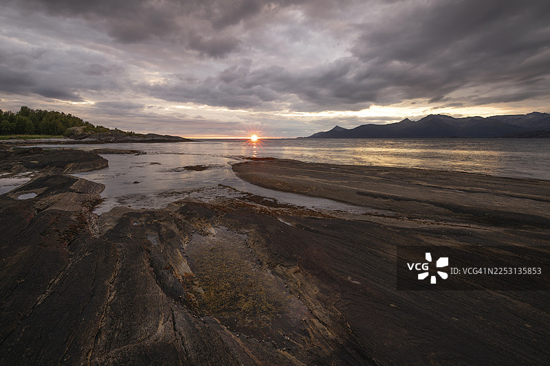 挪威诺德兰郡的韦斯特峡湾在博多附近呈现出戏剧性的氛围。傍晚的落日将深邃的云层染成红黄两色，崎岖的山崖和山峦倒映在宁静的峡湾中，呈现出令人惊叹的洛[卡]景观。图片素材