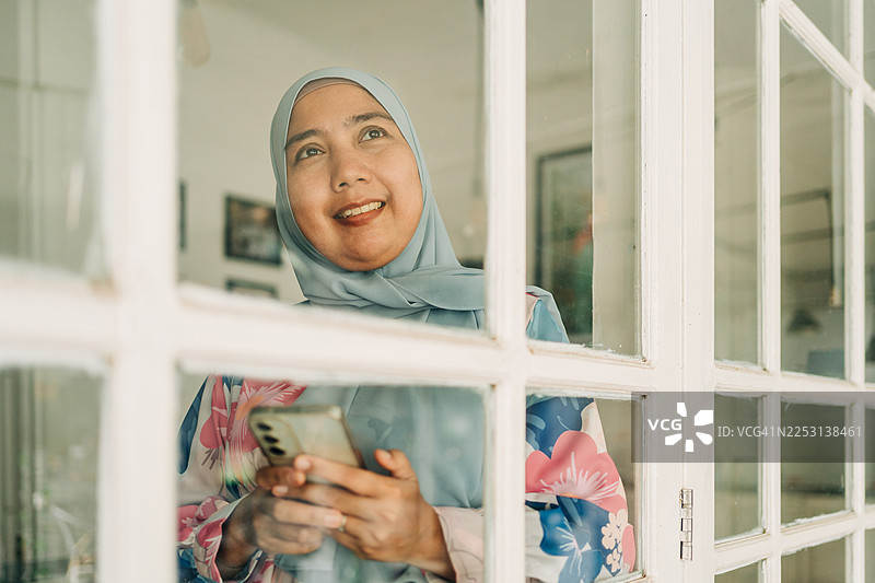 透过玻璃窗看到的亚洲女性使用手机的肖像图片素材