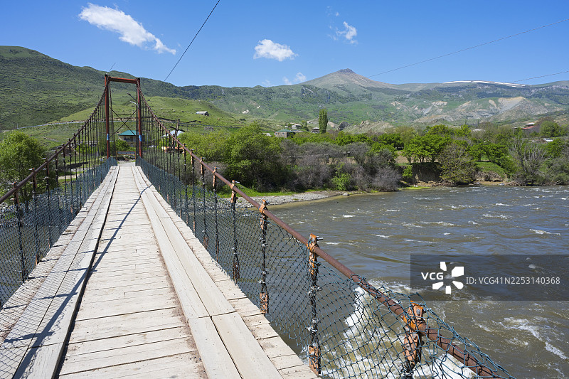 俯瞰一座横跨河流的悬索桥，背景是绿色山丘和山脉，位于格鲁吉亚萨姆茨赫-贾瓦赫季地区尼格里附近的库拉河图片素材