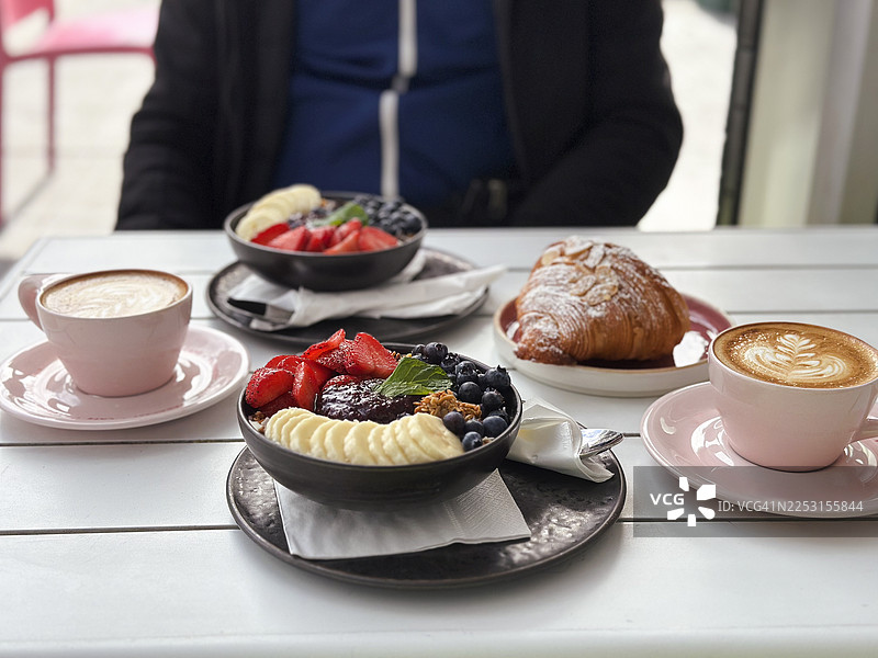 白色桌子上的卡布奇诺咖啡、羊角面包和水果碗的正面视图图片素材