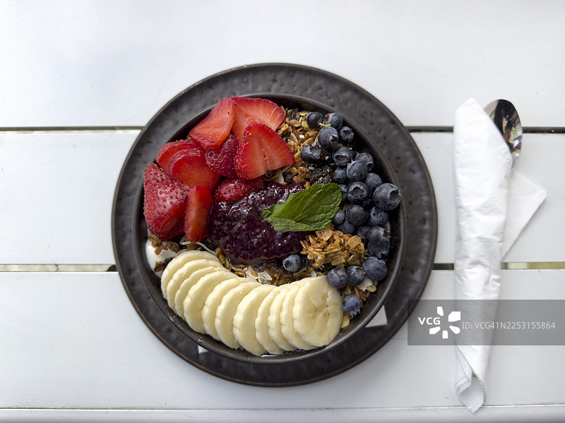 俯视角度拍摄的单一阿萨伊酸奶碗，配有新鲜草莓、蓝莓和香蕉，背景为白色。图片素材