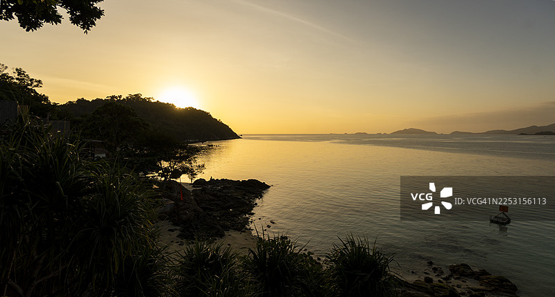 泰国沙敦岛丽贝岛日落海滩的日落景观，金色光芒倒映在平静的海面上，海岸线剪影清晰可见。图片素材