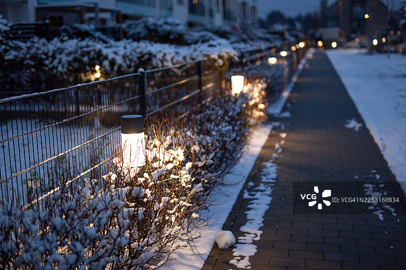 冬夜，雪后优雅的庭院里，人行道旁的一排灯图片素材