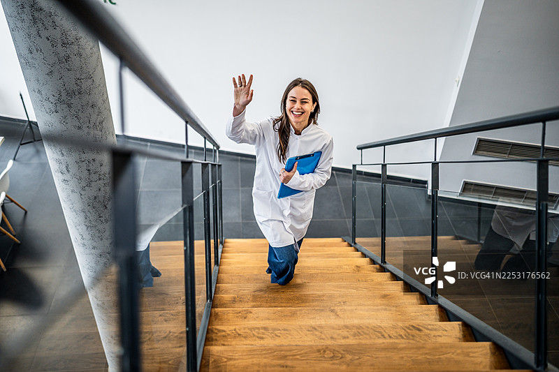 一位女性医护人员在走上楼梯时，带着愉快的笑容打着招呼图片素材