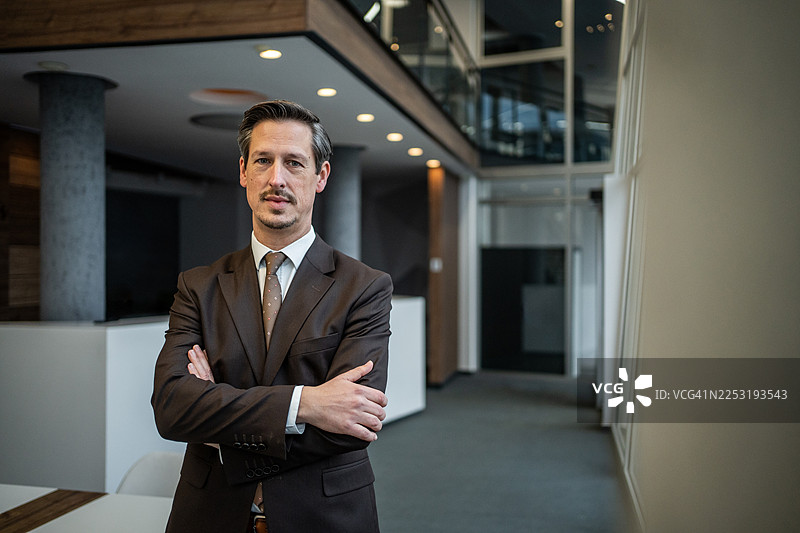专业的商人，双手抱臂，站立在现代办公室里图片素材