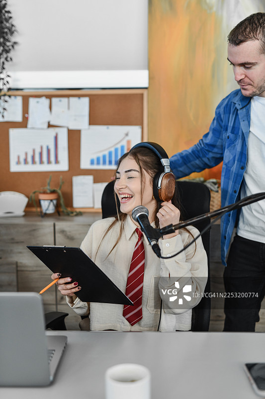 快乐的女主持人戴着耳机和麦克风在办公室进行访谈设置图片素材