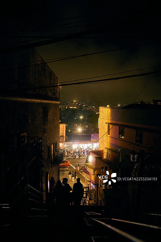 从高处俯瞰夜景，可以看到人们走在陡峭的街道上，进入一个繁忙、灯火通明的区域。图片素材