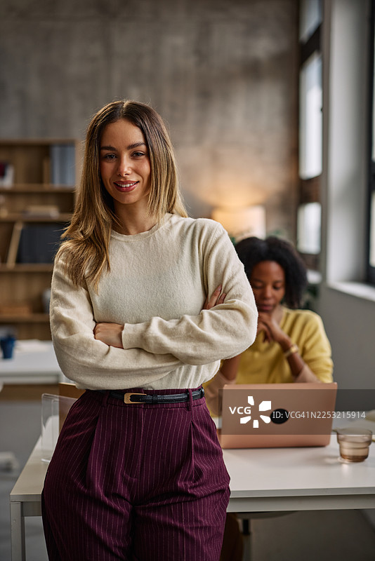 自信的女商人在办公室里，同事在一旁使用笔记本电脑工作图片素材