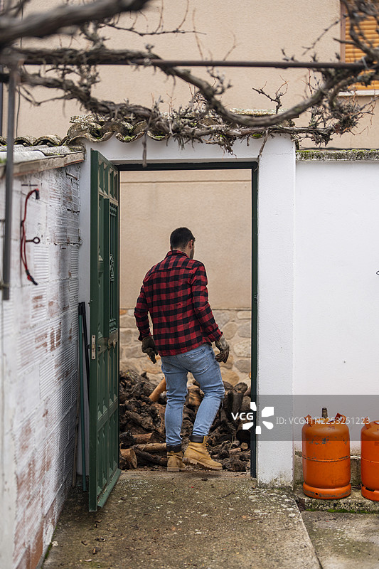 穿着格子衬衫的男人带着木柴进入储藏室图片素材