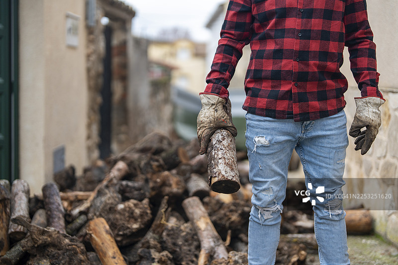 戴着工作手套、穿着格子衬衫的人在搬运木头图片素材