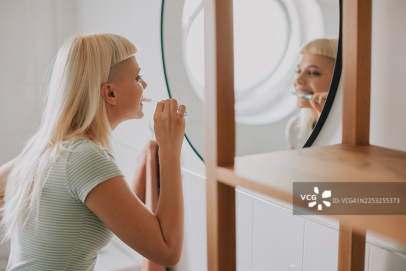 年轻的时尚女性在浴室刷牙，早晨例行公事，看着镜子图片素材