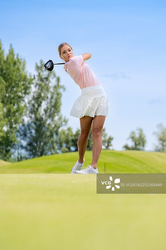 白种女性在郁郁葱葱的高尔夫球场上挥杆动作图片素材