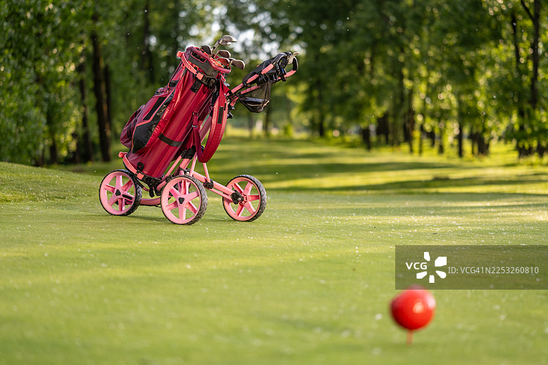 球道上带球杆的亮色高尔夫球包和红色发球座图片素材